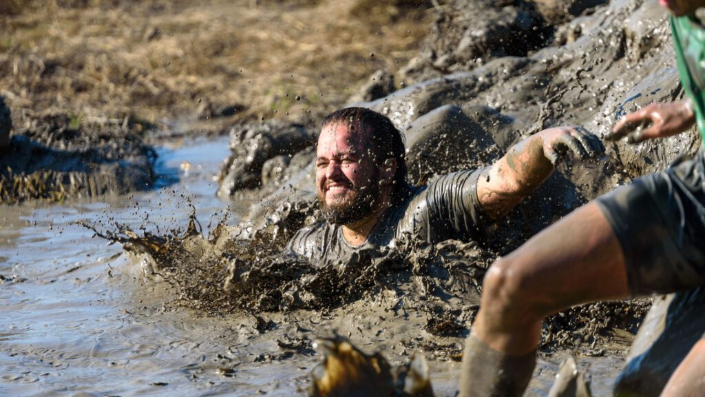 Man die lachend het water in glijd tijdens de strong family mud run
