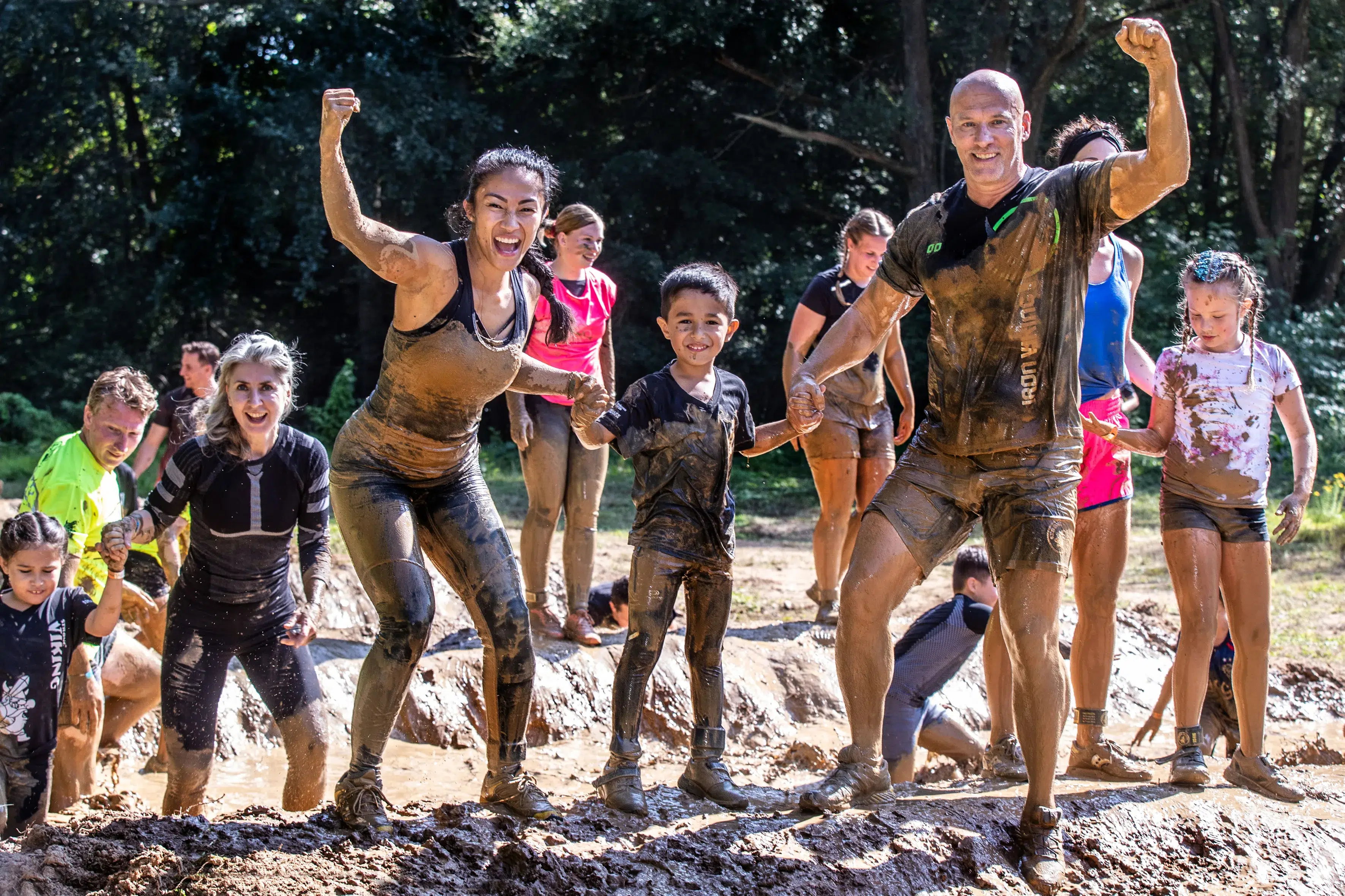 Kinderen en volwassenen die door de modder lopen en hun spierballen laten zien tijdens de Obstacle run Mud editie. (foto voor obstacle run kinderfeestje)